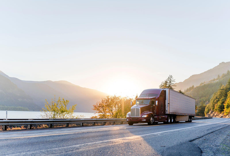 Big rig semi truck transporting commercial cargo in refrigerator semi trailer driving on the road along Columbia River with sunshine