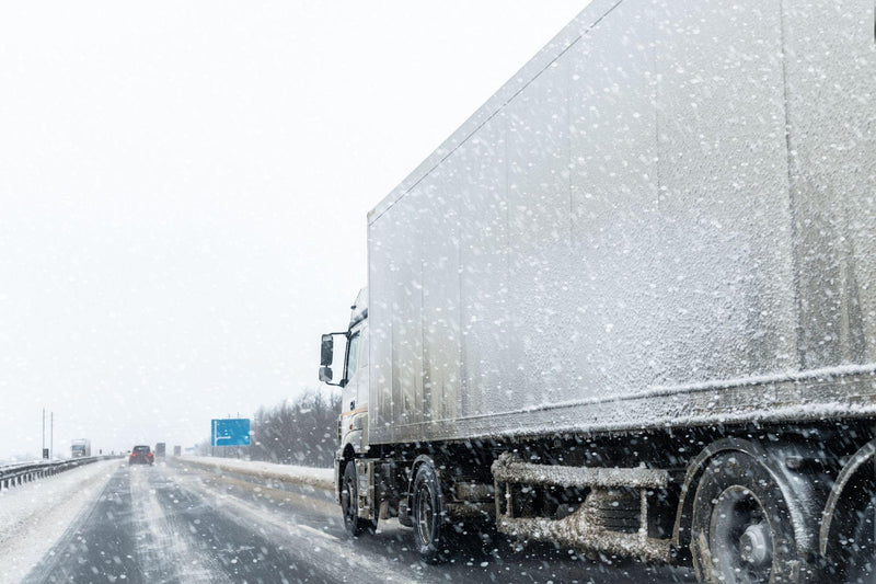 Cargo semi trailer truck moving fast on motorway road at heavy snowfall in winter.