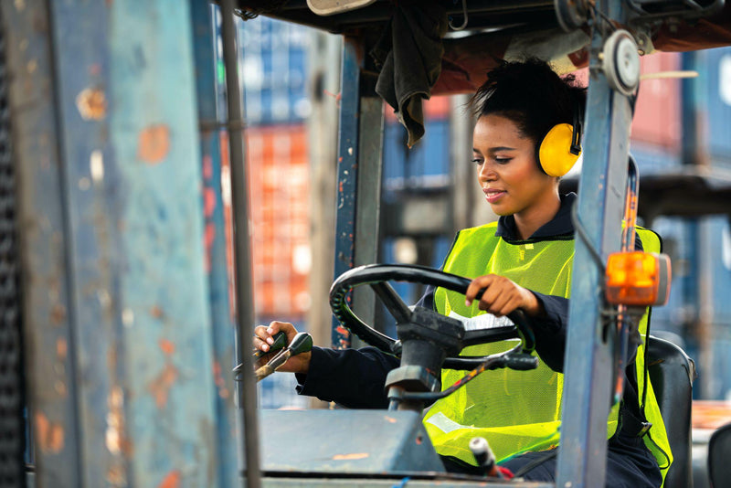 Female worker driving forklift in industrial container warehouse.