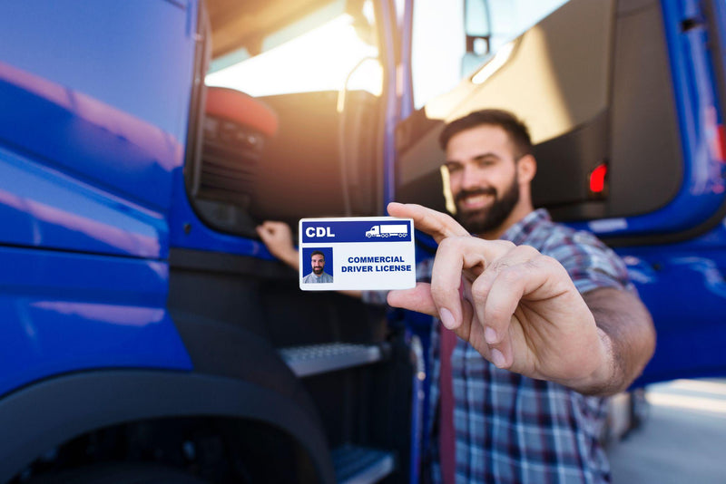 Middle aged truck driver standing by his truck and showing his commercial driver license.