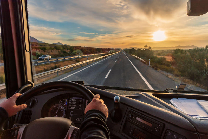 View from the driver's seat of a truck of the highway and a landscape of fields at dawn